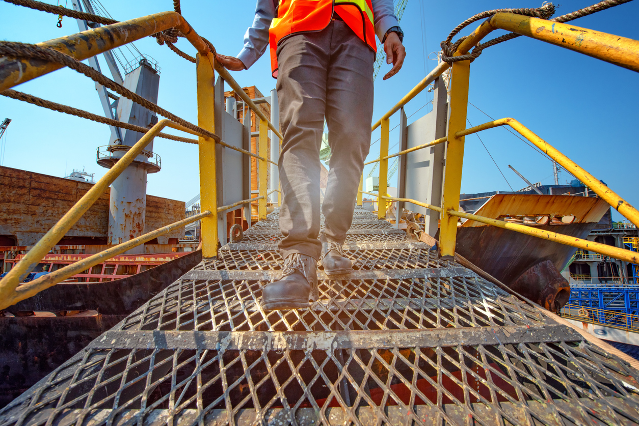 Maritime worker in a safety vest crossing a metal gangway between cargo ships at a dock, illustrating the offshore and dock hazards handled by the Houston maritime injury lawyers at Attorney Brian White Personal Injury Lawyers